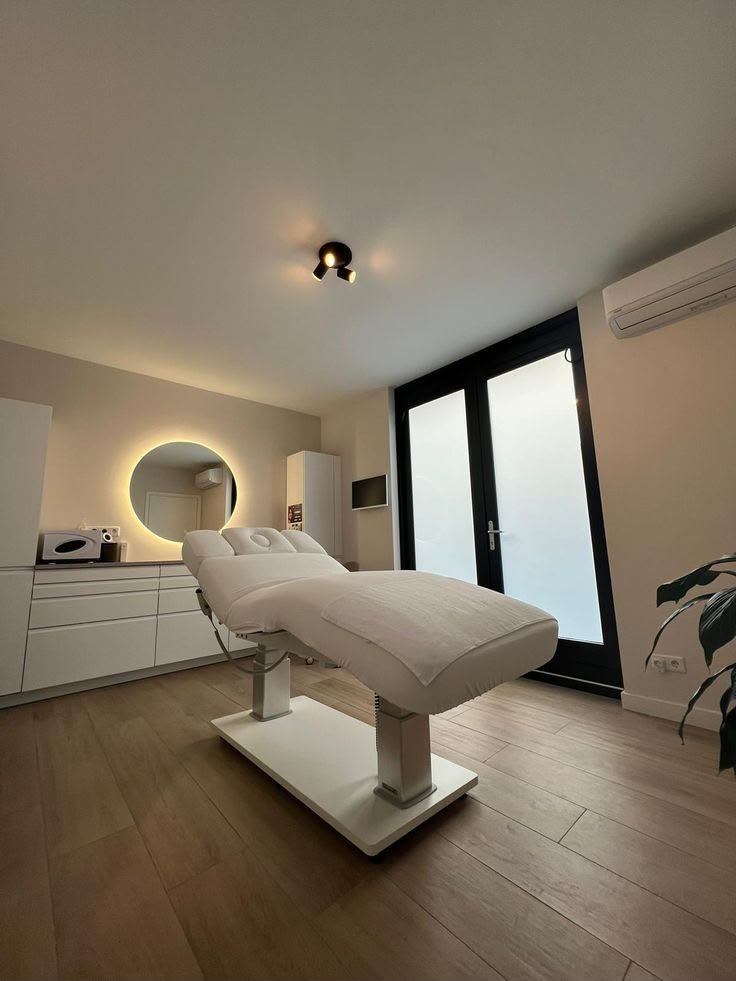 Sala de estética luminosa con espejo redondo retroiluminado y mobiliario blanco